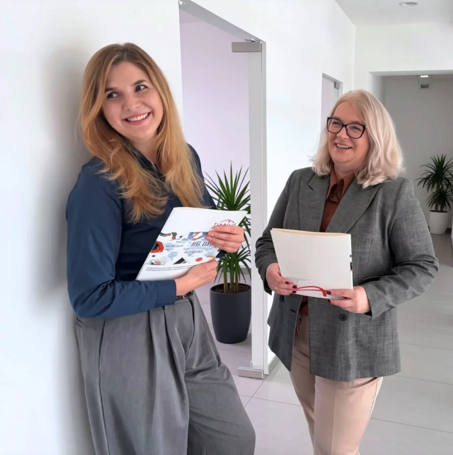 Dwie pracownice Fiabilis rozmawiają w biurze, trzymając dokumenty
